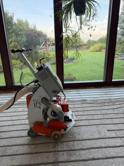 Bodenfräse mit angeschlossenem Absaugschlauch auf gefrästem Estrich im Wintergarten